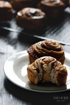 two cinnamon rolls on a white plate next to some muffins in the background