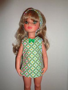 a doll with blonde hair wearing a green dress and headband, standing in front of a white wall