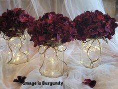 three mason jars filled with purple flowers and fairy lights