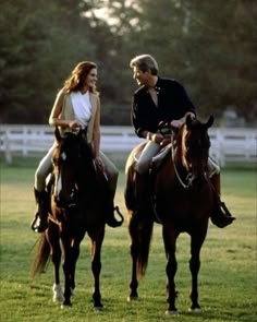 a man and woman riding on the backs of brown horses in a grassy field next to each other