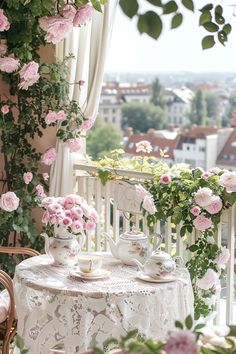 a table with pink flowers and tea cups on it in front of a balcony overlooking the city