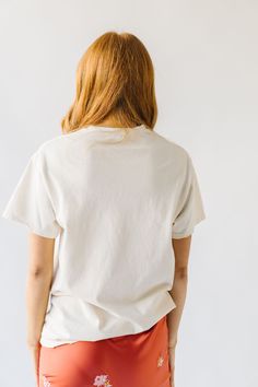 a woman with her back turned to the camera, wearing an orange skirt and white t - shirt