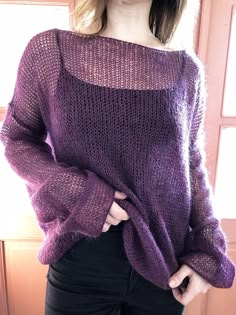 a woman standing in front of a window wearing a purple sweater