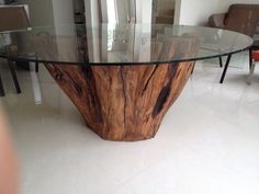 a glass table with a wooden base in the middle of a white floored room