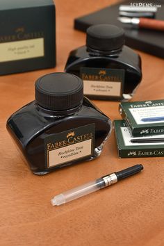 three ink bottles and two pens sitting on a table next to some other writing supplies