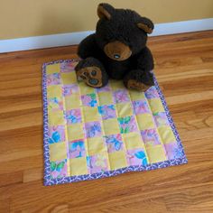 a black teddy bear sitting on top of a yellow and pink quilted mat with flowers