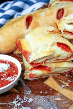 several pieces of pizza sitting on top of a cutting board next to a bowl of sauce