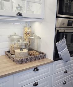 a kitchen with white cabinets and wooden counter tops, including jars filled with food in front of an oven