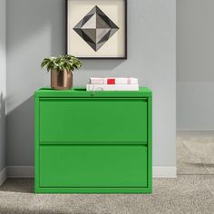 a green filing cabinet in an empty room with a plant on top and pictures above it