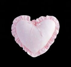 a pink heart shaped pillow with ruffles hanging from it's side on a black background