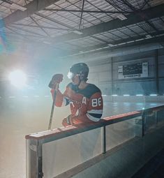 a hockey player sitting on a bench in the middle of an indoor rink holding a bat