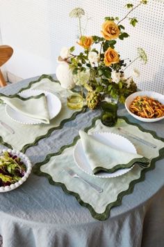 the table is set with plates, bowls and flowers