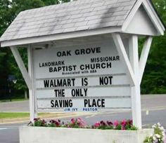 a sign that is on the side of a road in front of flowers and trees