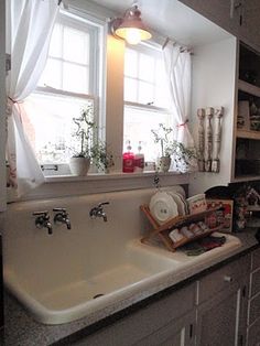 a kitchen sink sitting under a window next to a shelf filled with pots and pans