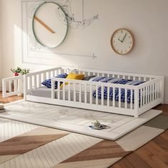 a white crib with blue and yellow pillows in front of a clock on the wall