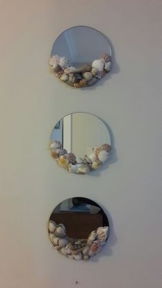 three circular mirrors mounted to the side of a wall with seashells on them