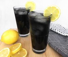 two glasses filled with black liquid next to sliced lemons