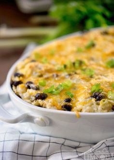 a casserole dish with black beans, cheese and green onions on the side