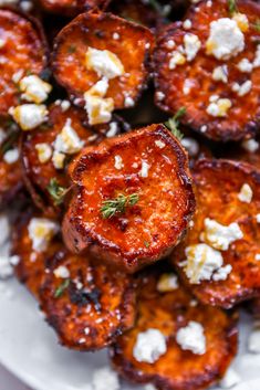 a white plate topped with sweet potatoes covered in feta cheese and garnished with fresh herbs