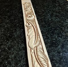 an intricately carved wooden object on a black counter top with a white feather in the center