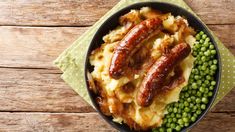 two sausages on top of mashed potatoes and peas