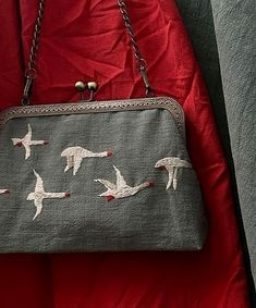 a purse with birds painted on it sitting on a red cloth covered bedding area