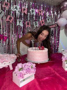 a woman blowing out candles on a pink cake