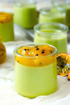 two jars filled with green and yellow liquid on top of a white cloth next to sliced oranges