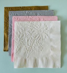 three napkins with embroidered flowers on them, one in pink and one in grey