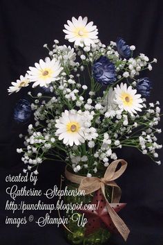 a vase filled with white and blue flowers on top of a black tableclothed background