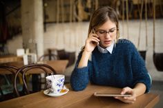 a woman sitting at a table talking on her cell phone while holding a tablet computer