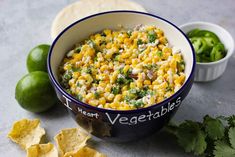 a bowl filled with corn and salsa next to tortilla chips, lime wedges and cilantro