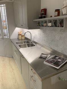 a kitchen with stainless steel counter tops and white cupboards, along with a magazine on the sink