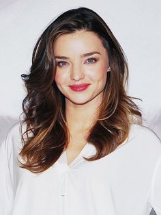 a woman with long brown hair wearing a white shirt and red lipstick is smiling at the camera