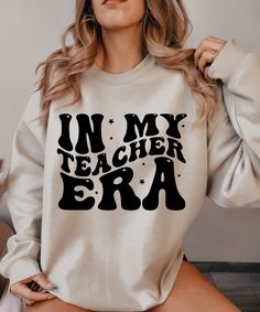 Step back in time and immerse yourself in the nostalgic world of teaching with our In My Teacher Era sweatshirt design in retro style. The classic black hue of the sweatshirt is beautifully accented by the playful retro design, instantly evoking memories of bygone eras. This isn't just any ordinary sweatshirt - it's a heartfelt expression of gratitude towards the teachers who have shaped us. Whether you're a seasoned educator reminiscing about the good ol' school days or someone who holds a spec Retro Slogan Tops For School, Retro School Tops With Slogan, Retro Cotton Sweatshirt With Slogan, Vintage Cotton Sweatshirt With Slogan, Sublimation Shirts, Retro Sweatshirts, My Teacher, Sublime Shirt, Funny Teacher