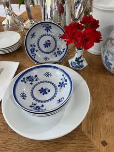 blue and white plates with red flowers in vases on wooden table top next to silverware