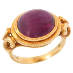 A fantastic Estate rhodolite garnet ring! This 18kt yellow gold piece is bold in size and shape and features a striking rhodolite garnet cabochon at its center. The incredible stone displays a natural reddish-purple color with excellent clarity. A knotted gold bezel setting holds the stone in place, creating a wonderful cut out design that showcases the gemstone beautifully. Finishing the design is a smoothly polished band at the back and stamped inside of the shank is "18k" along with a maker's Luxury Ruby Ring With Oval Cabochon, Luxury 14k Gold Ruby Cabochon Ring, Fine Jewelry Ruby Oval Cabochon Ring, Rhodolite Garnet Ring, Reddish Purple, Cabochon Ring, Garnet Ring, Rhodolite Garnet, Gold Piece