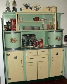 an old fashioned kitchen with green cabinets and white cupboards on the top shelf is filled with dishes