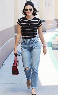 a woman in black and white striped shirt walking down the street with a red purse