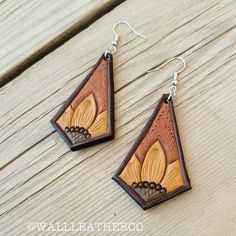 two wooden earrings with flowers on them sitting on top of a wooden table next to a piece of wood