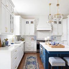 a kitchen with white cabinets, blue and white rug and chandelier hanging from the ceiling