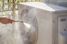 a person is spraying water on an air conditioner that's outside in the daytime