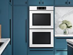 a kitchen with blue cabinets and white counter tops, two ovens are built into the wall