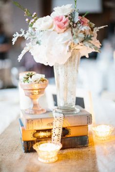 a vase filled with white flowers sitting on top of books next to candles and tea lights