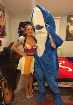 a woman standing next to a giant shark mascot in a room with guitars on the floor