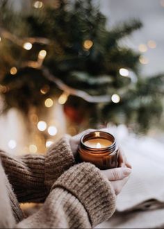 a person holding a candle in their hand near a christmas tree with lights on it