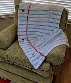 a crocheted blanket sitting on top of a chair next to a window with blinds