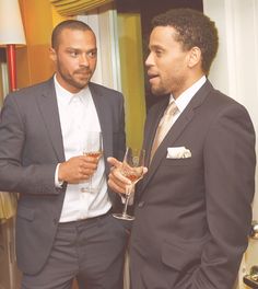 two men standing next to each other holding wine glasses