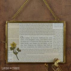 a framed book page with flowers hanging from it's sides on a chain attached to the wall