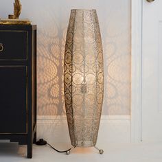 a tall vase sitting on top of a table next to a black cabinet and lamp